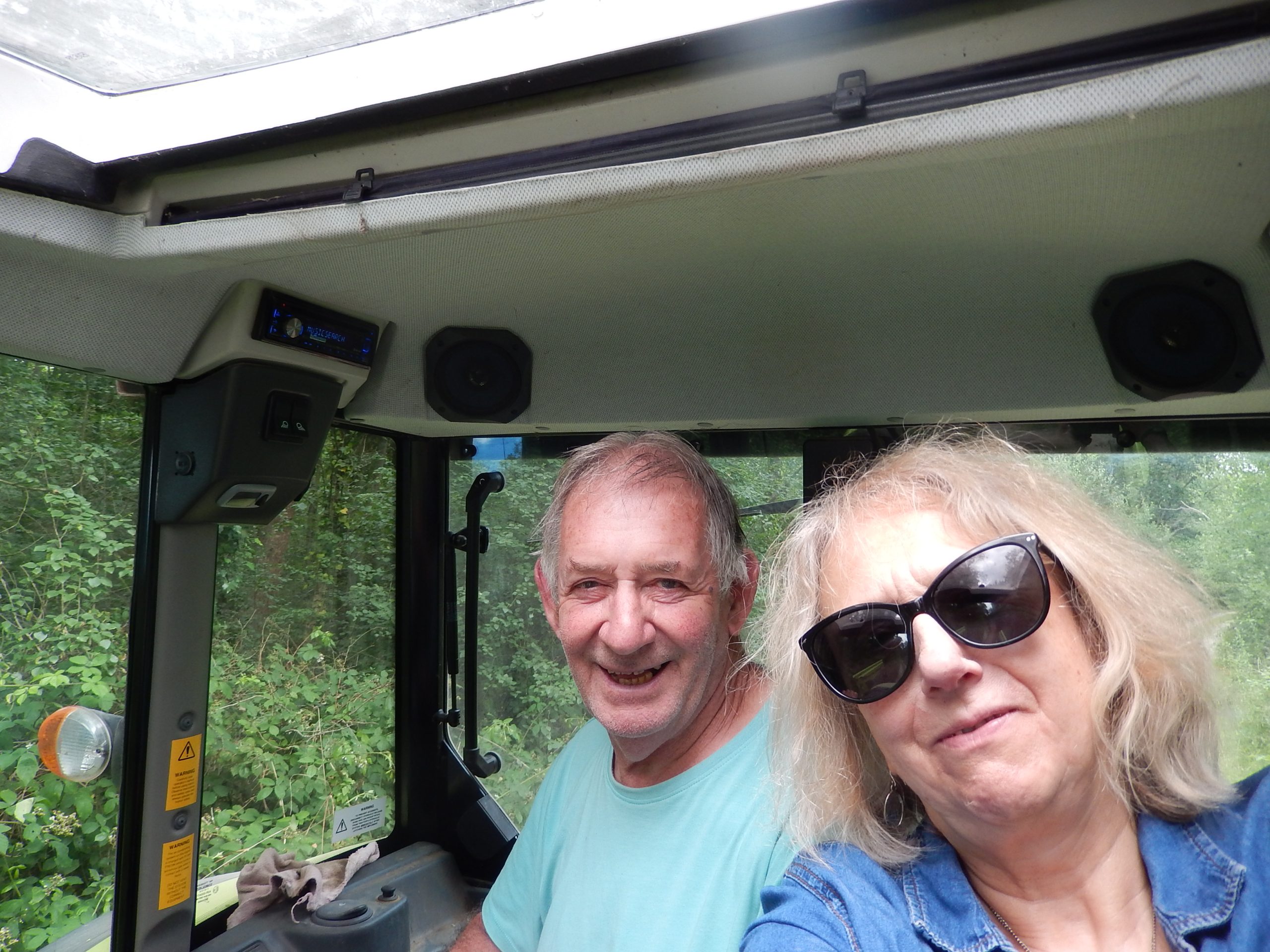 Steve and Helen sitting inside a green tractor cab, smiling for the camera before starting verge maintenance work in Howes Wood.